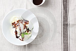 Vanilla andÂ pistachio ice cream with chocolate sauce in a bowl on a plate on a linen textile